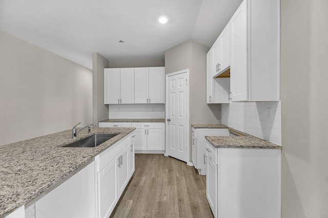 kitchen featuring white cabinets, sink, light wood-type flooring, tasteful backsplash, and light stone counters