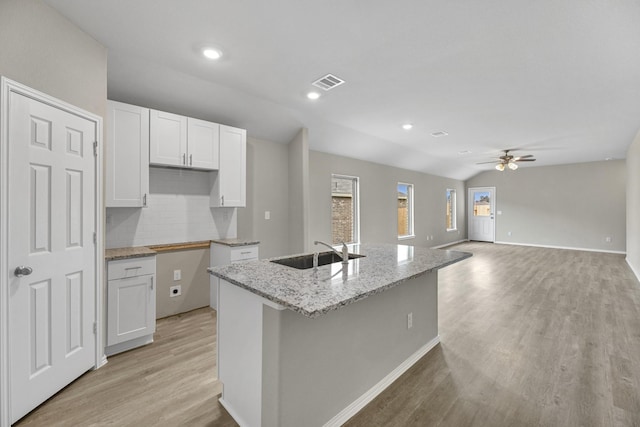 kitchen with light wood-type flooring, ceiling fan, sink, white cabinets, and an island with sink