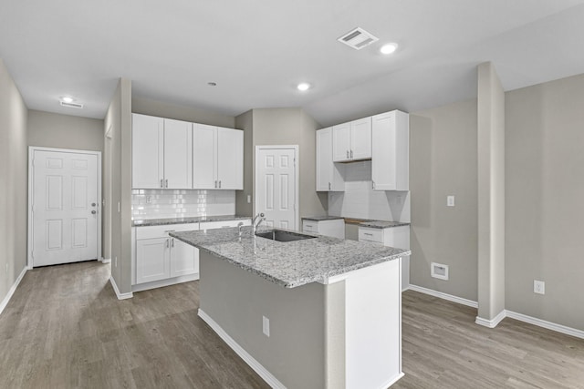 kitchen with white cabinets, light stone countertops, an island with sink, and light wood-type flooring