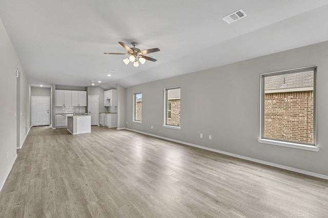 unfurnished living room featuring a wealth of natural light, ceiling fan, and light hardwood / wood-style floors