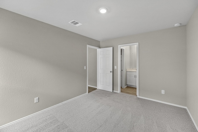 unfurnished bedroom featuring light carpet and ensuite bath