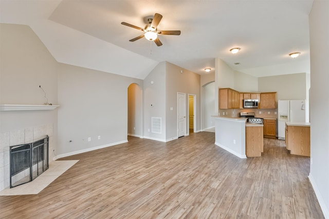 kitchen with stainless steel appliances, vaulted ceiling, a tiled fireplace, ceiling fan, and light hardwood / wood-style flooring