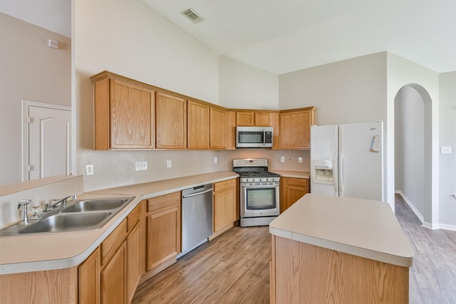 kitchen featuring appliances with stainless steel finishes, light hardwood / wood-style floors, a center island, a towering ceiling, and sink