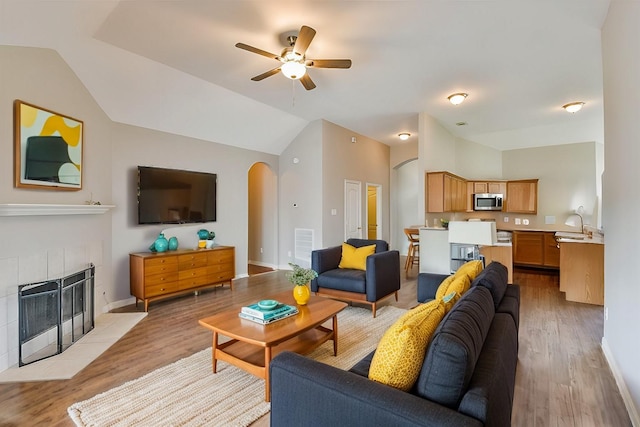 living room featuring vaulted ceiling, a fireplace, light wood-type flooring, and ceiling fan