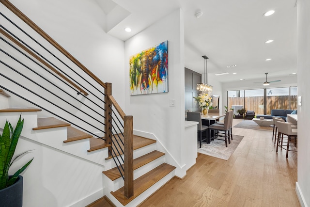 staircase with hardwood / wood-style flooring and ceiling fan with notable chandelier