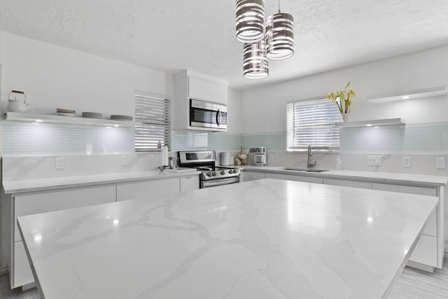 kitchen with stainless steel appliances, sink, white cabinets, light stone counters, and pendant lighting