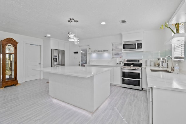 kitchen featuring a center island, hanging light fixtures, white cabinetry, appliances with stainless steel finishes, and sink