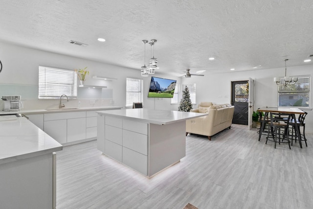 kitchen with white cabinets, decorative light fixtures, sink, and a kitchen island