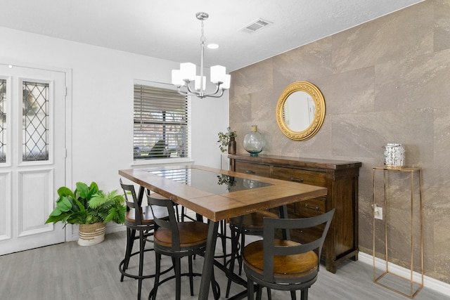 dining room with tile walls, an inviting chandelier, and light hardwood / wood-style floors