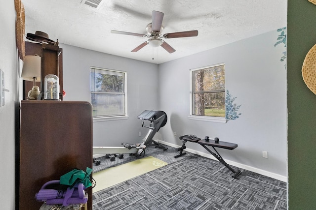 workout area with ceiling fan, a textured ceiling, and dark colored carpet