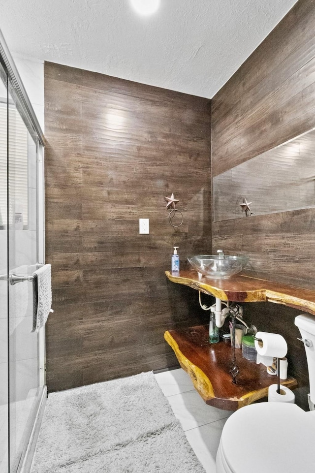 bathroom with sink, a textured ceiling, a shower with shower door, toilet, and tile patterned floors