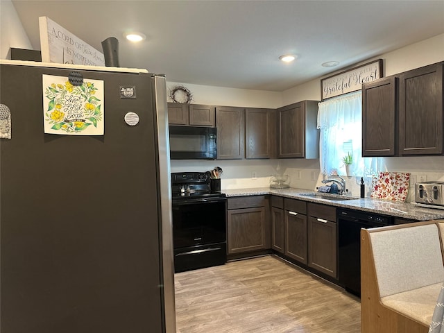 kitchen featuring light stone countertops, dark brown cabinetry, sink, black appliances, and light hardwood / wood-style floors