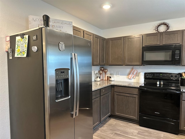 kitchen with dark brown cabinets, light wood-type flooring, light stone counters, and black appliances