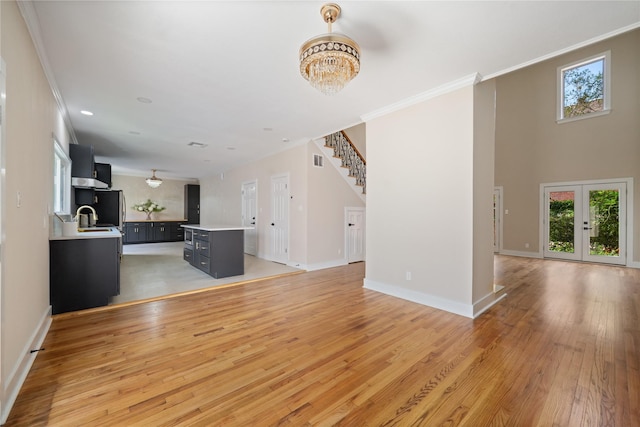 unfurnished living room with sink, french doors, a notable chandelier, light wood-type flooring, and ornamental molding