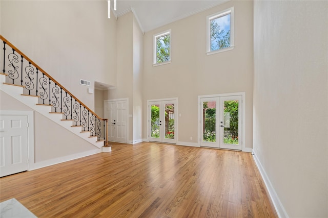 unfurnished living room with french doors, a towering ceiling, a healthy amount of sunlight, and hardwood / wood-style flooring