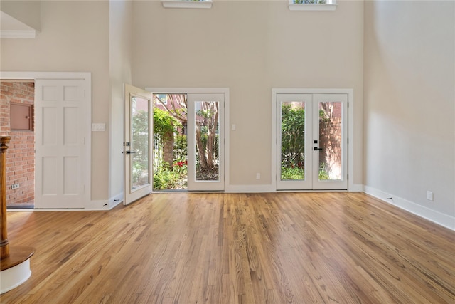 unfurnished living room featuring light hardwood / wood-style floors, a high ceiling, and french doors