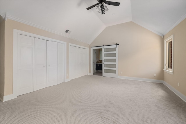 unfurnished bedroom featuring ceiling fan, a barn door, crown molding, carpet floors, and lofted ceiling