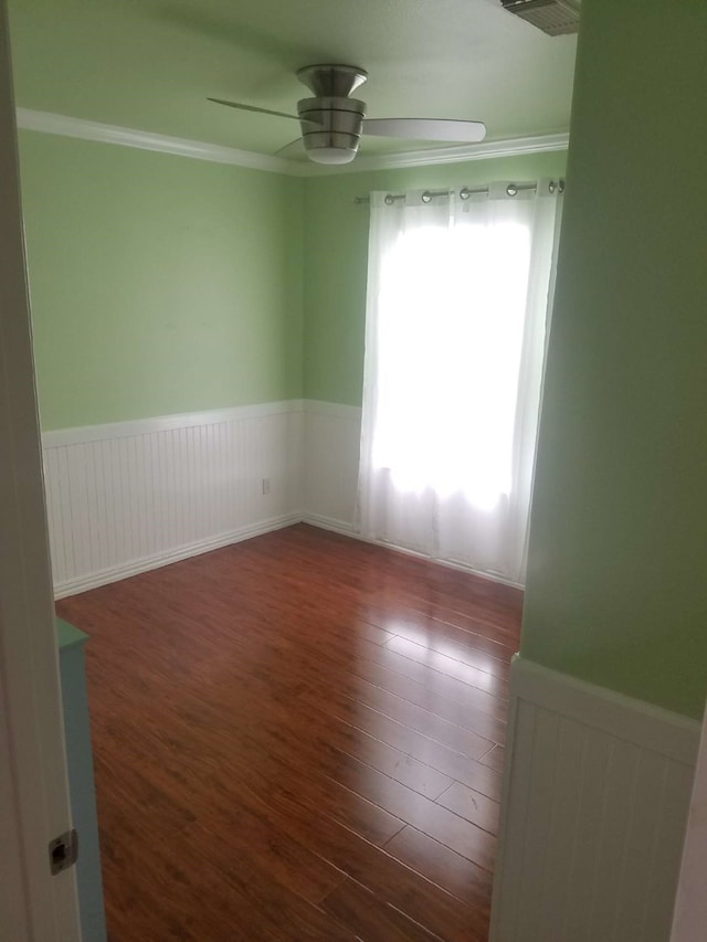 empty room with a wainscoted wall, ceiling fan, ornamental molding, and wood finished floors