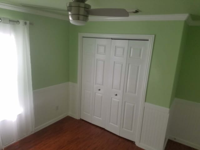 unfurnished bedroom with a ceiling fan, a closet, wainscoting, and wood finished floors