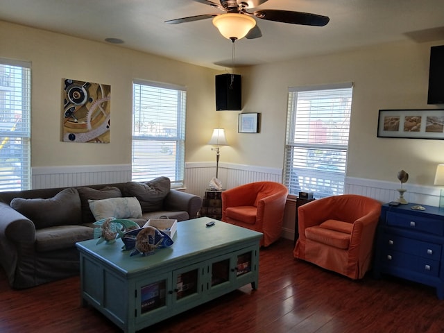 living room featuring a wainscoted wall, dark wood-style floors, a wealth of natural light, and a ceiling fan