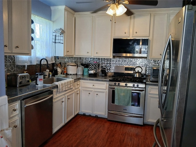 kitchen with stainless steel appliances, a sink, white cabinets, dark wood-style floors, and dark countertops