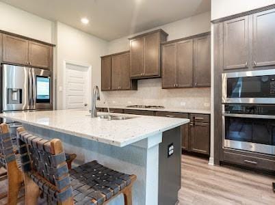 kitchen featuring a kitchen bar, appliances with stainless steel finishes, sink, light hardwood / wood-style floors, and an island with sink