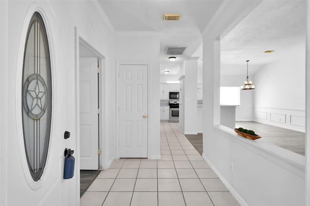 hallway featuring light tile patterned floors, a notable chandelier, and ornamental molding