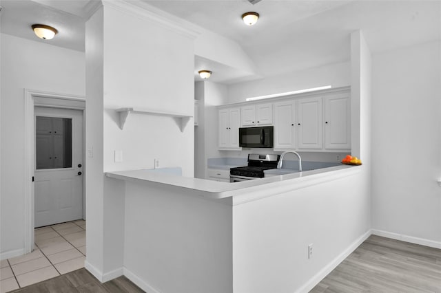 kitchen featuring kitchen peninsula, stainless steel gas range oven, light tile patterned floors, white cabinetry, and lofted ceiling