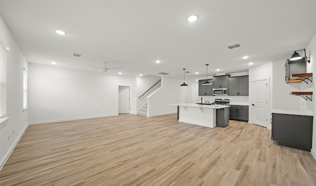 kitchen featuring appliances with stainless steel finishes, pendant lighting, an island with sink, and light wood-type flooring