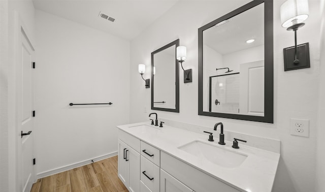 bathroom with a tile shower, wood finished floors, a sink, and visible vents