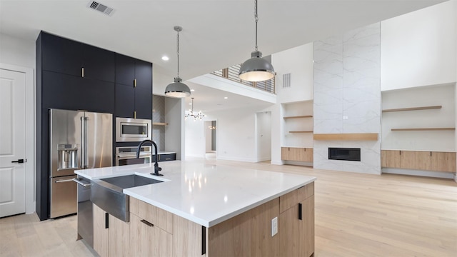 kitchen with appliances with stainless steel finishes, sink, a fireplace, hanging light fixtures, and an island with sink