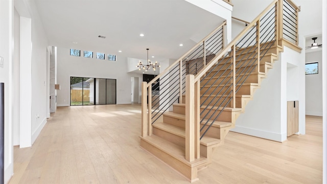 stairs featuring a towering ceiling, ceiling fan with notable chandelier, and hardwood / wood-style flooring