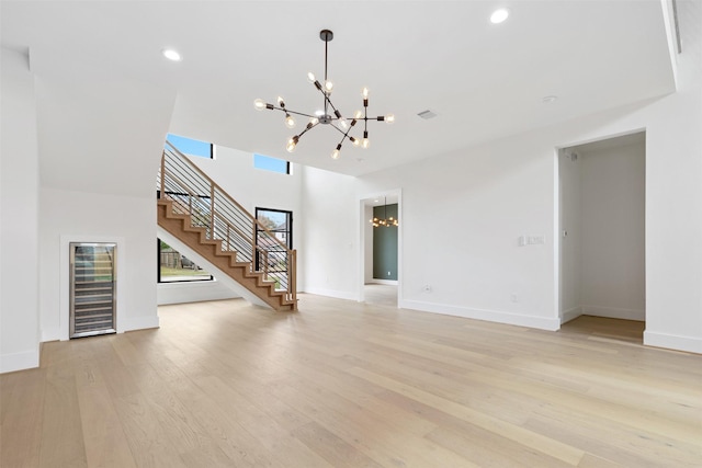 unfurnished living room featuring light hardwood / wood-style flooring, a high ceiling, and an inviting chandelier