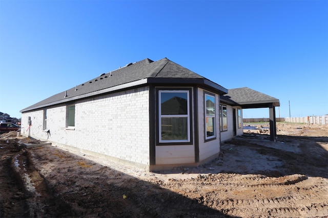 view of side of home with brick siding and roof with shingles