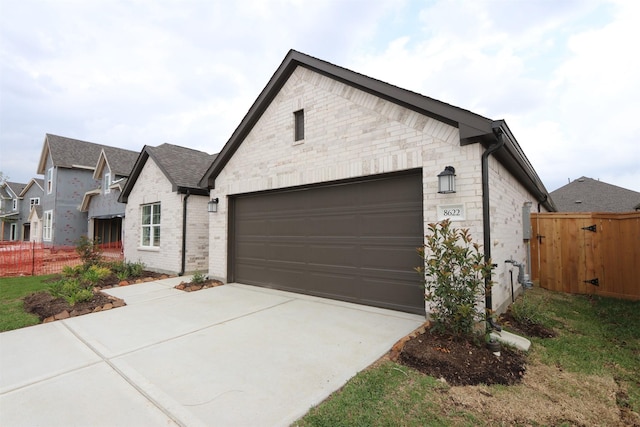 view of front facade with driveway, stone siding, fence, a garage, and brick siding