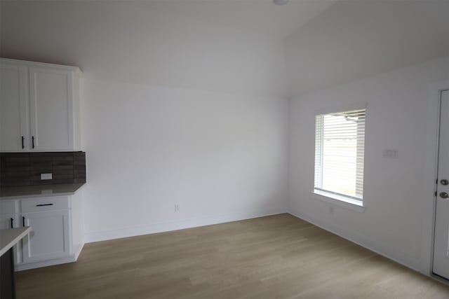 unfurnished dining area with vaulted ceiling, baseboards, and light wood-type flooring