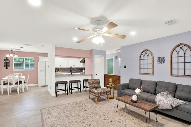 living room featuring light hardwood / wood-style flooring, ceiling fan with notable chandelier, and sink