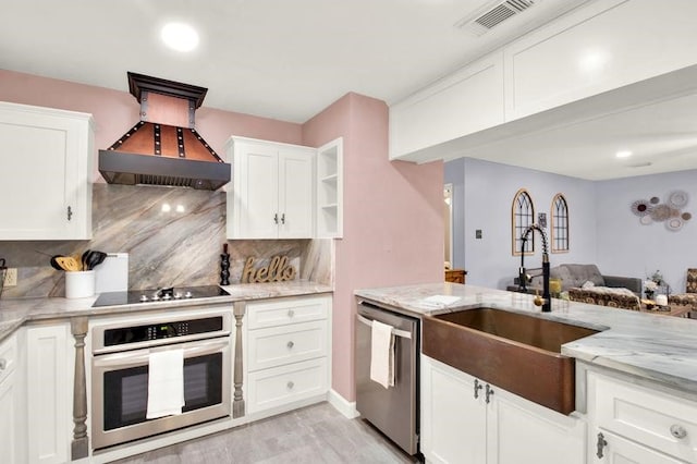 kitchen featuring light stone countertops, tasteful backsplash, appliances with stainless steel finishes, white cabinets, and custom exhaust hood