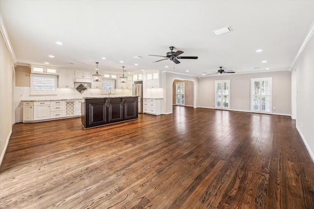 unfurnished living room with ceiling fan, a healthy amount of sunlight, dark hardwood / wood-style floors, and ornamental molding