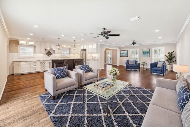 living room featuring arched walkways, crown molding, recessed lighting, visible vents, and wood finished floors