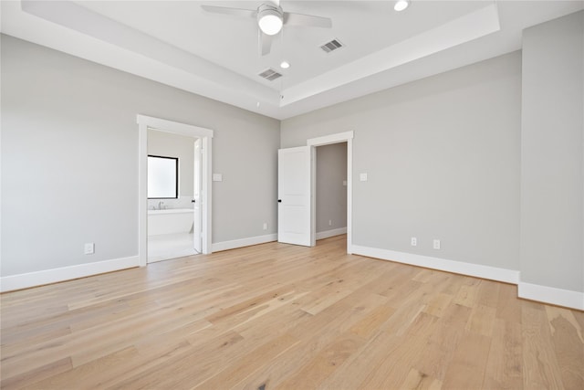 empty room with a raised ceiling, ceiling fan, and light hardwood / wood-style flooring