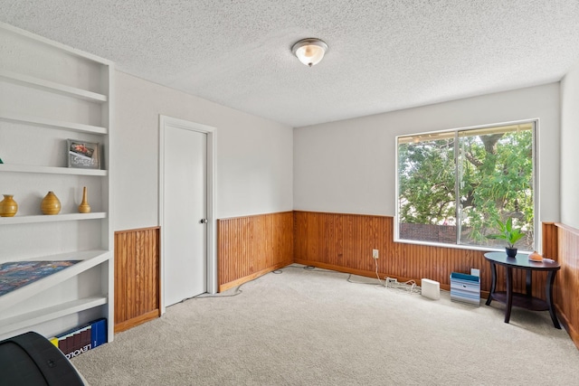 misc room featuring built in shelves, light colored carpet, a textured ceiling, and wooden walls