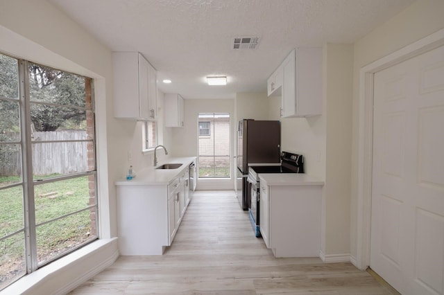 kitchen with white cabinetry, sink, black / electric stove, light hardwood / wood-style floors, and a textured ceiling