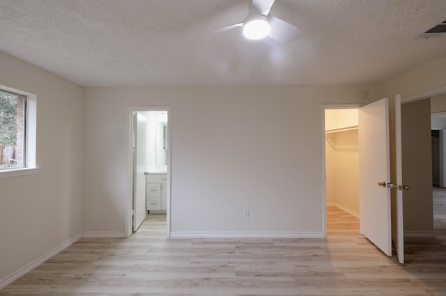 unfurnished bedroom with ensuite bathroom, light hardwood / wood-style flooring, ceiling fan, a spacious closet, and a closet