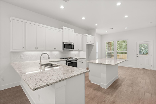 kitchen featuring kitchen peninsula, light stone counters, stainless steel appliances, light hardwood / wood-style flooring, and a kitchen island