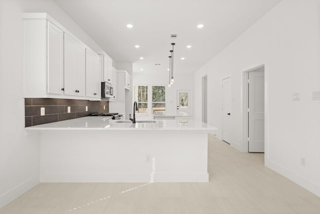 kitchen featuring white cabinets, stainless steel microwave, a peninsula, light countertops, and backsplash