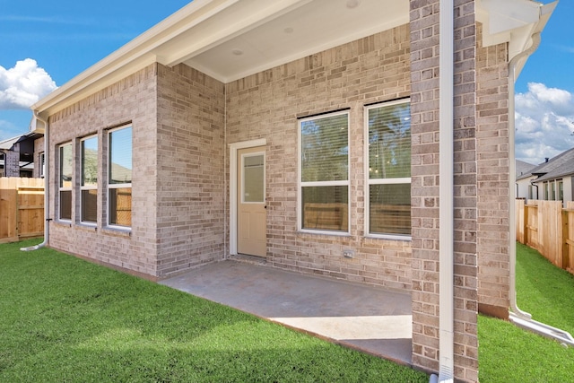 property entrance featuring a yard, a patio area, brick siding, and fence