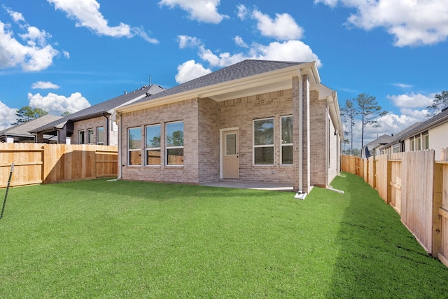 rear view of house featuring a fenced backyard, brick siding, a shingled roof, a yard, and a patio area