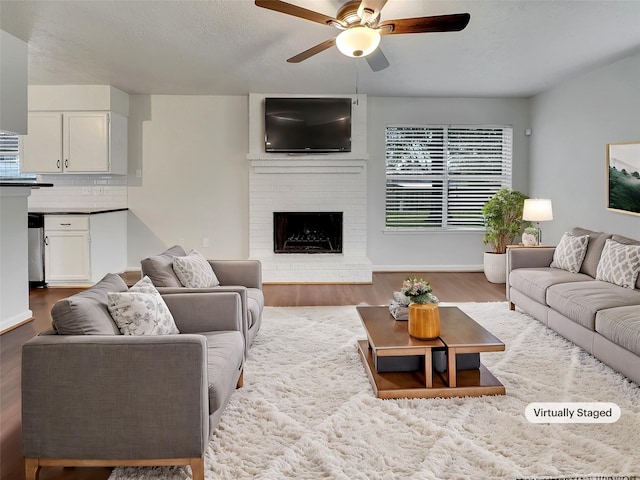 living room featuring ceiling fan, wood-type flooring, and a brick fireplace