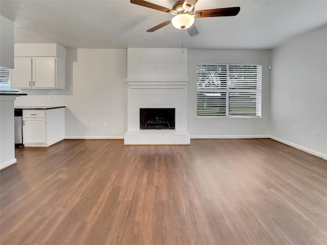 unfurnished living room with ceiling fan, a fireplace, wood-type flooring, and a textured ceiling